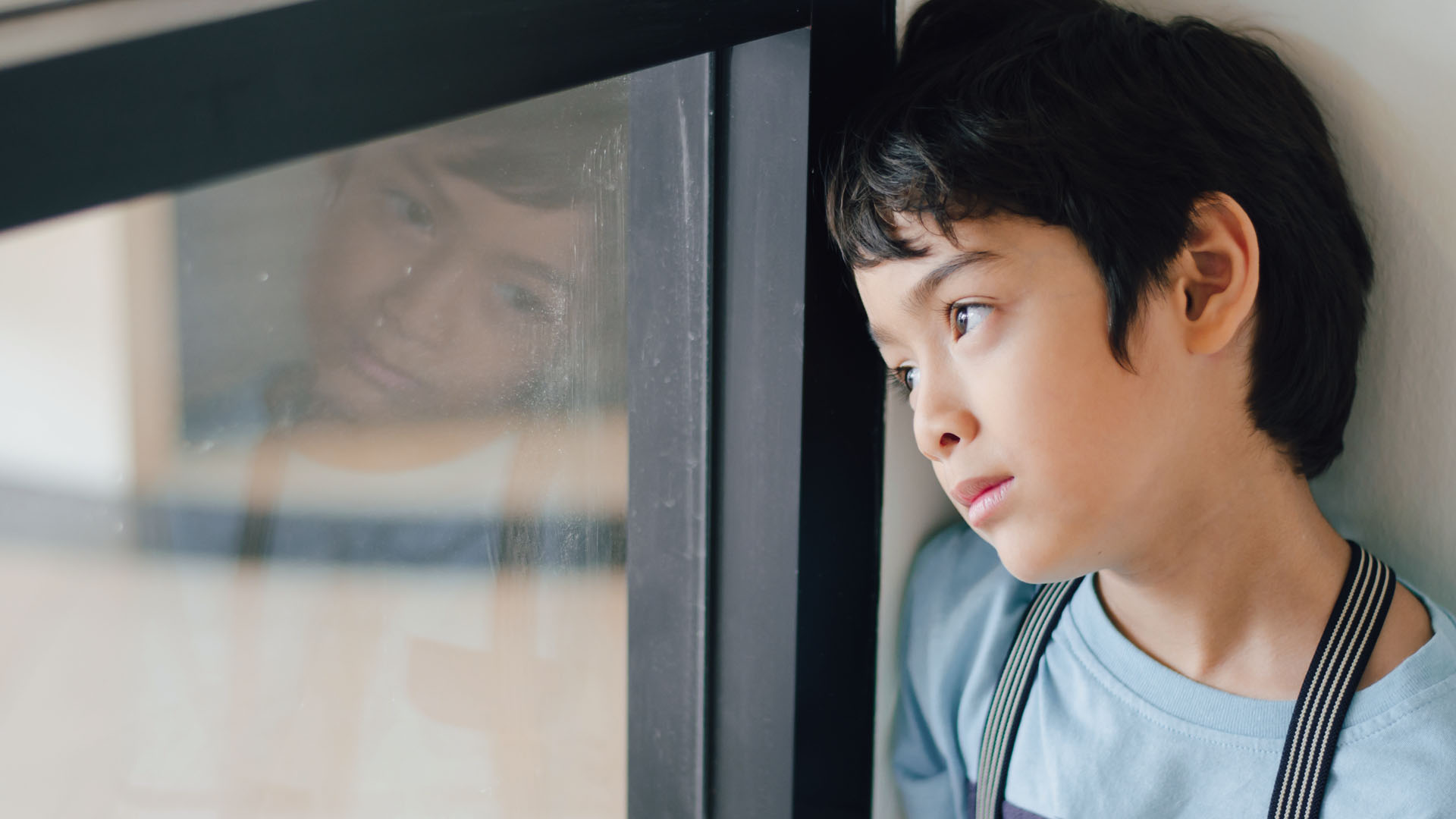 Boy gazing distantly out of a window.